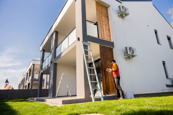 Man wearing casuals painting wooden columns of modern apartment against sky during sunny day